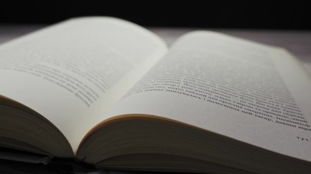 Close up view of white pages turning rapidly on an open book placed on a dark wooden surface. Concept of fast learning, academic research, history, and the power of knowledge.