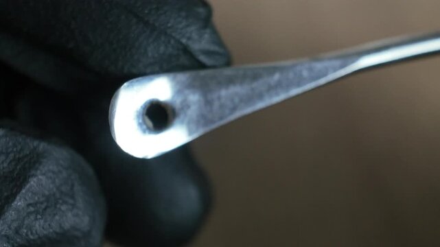 Close up macro shot of a stainless steel ear curette tool used for personal earwax removal, cleaning, and auditory hygiene held by gloved hands.