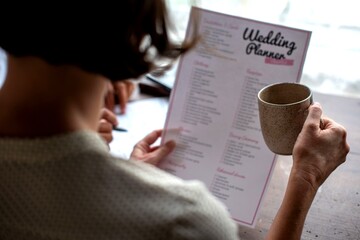 Naklejka premium Person holding a wedding planner and a coffee mug at a table.