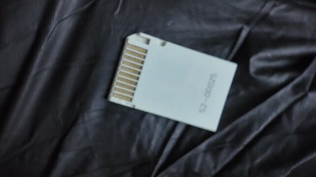Close up perspective of a white card adapter converting MicroSD to Memory Stick Pro Duo format, showing the gold contact pins on a dark background.