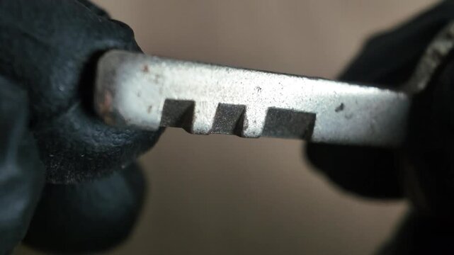 An extreme macro shot of hands in black gloves holding and demonstrating a vintage silver safe deposit box key with distinct square cut notches.