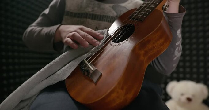 Boy Wipes Dust Cleaning Ukulele Instrument in Home Studio. 4K 10-bit