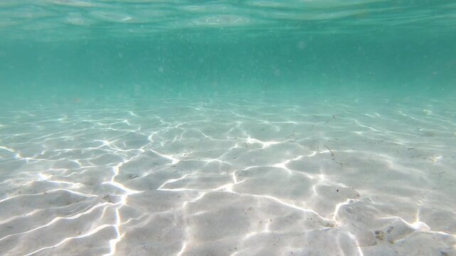 Underwater slow motion view of sunlight caustics on sandy seabed, shimmering light patterns moving across the ocean floor in clear turquoise Mediterranean water, natural abstract texture