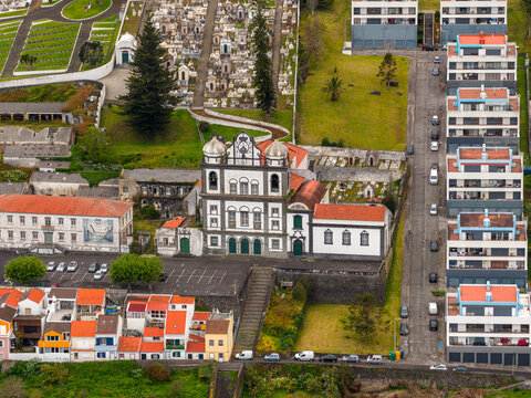 Aerial view of the historic Igreja de Nossa Senhora das Angustias surrounded by traditional houses, a cemetery, and modern apartment buildings in Horta, Acores, Portugal.