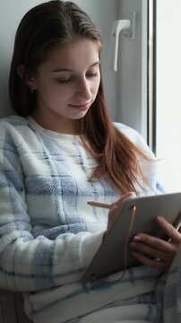 Teenage Girl In Pajamas Sits On A Windowsill Reading Notes In A Notebook, Vertical Video