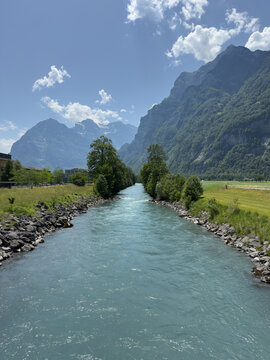 Turquoise Alpine River Channel Flowing Between Rocky Banks With Mountain Peaks in Glarus Switzerland