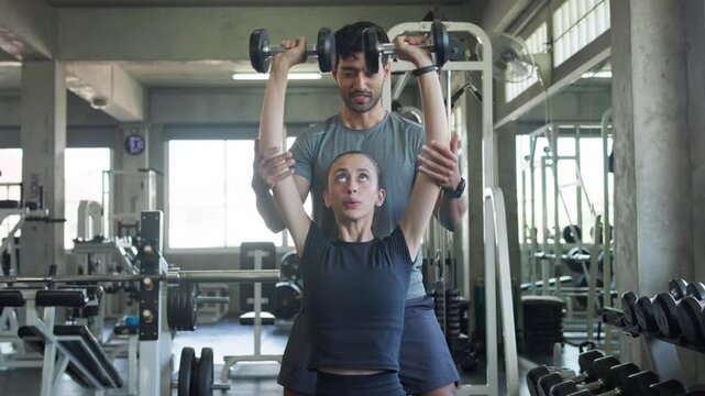 Fitness training session a coach assisting a woman with dumbbell exercises in a modern gym environment