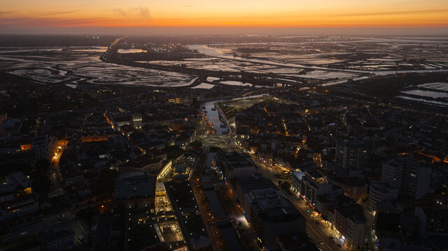Aerial view of Aveiro city at sunset with illuminated streets, canals, and surrounding wetlands in Portugal.