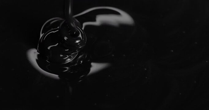 Black viscous liquid fast spiral. Close-up of thick black fluid flowing in rapid swirling spirals with white highlights.