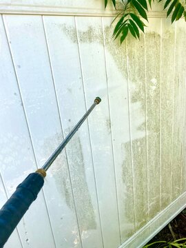 Power washing dirt off of white fence