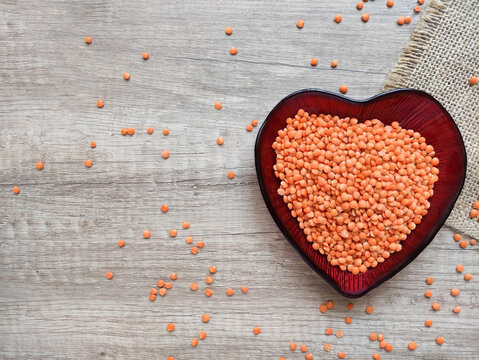 Red lentils in a decorative heart-shaped bowl on a brown wooden background. Healthy plant-based food, nutritious ingredient, top view, soft lighting.