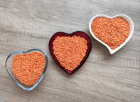 Red lentils in a decorative heart-shaped bowl on a brown wooden background. Healthy plant-based food, nutritious ingredient, top view, soft lighting.