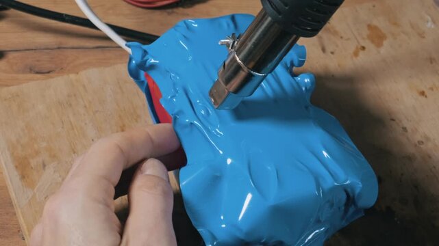 A person uses a hot air gun to tightly shrink blue PVC tubing around a custom lithium battery pack on a workbench. Concept of DIY electronics, energy storage, and engineering.