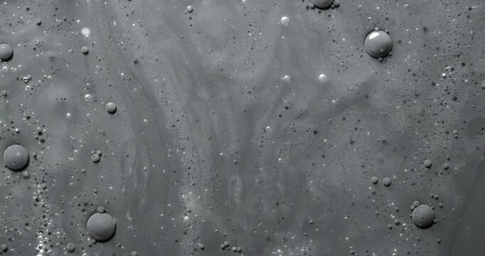Black bubbly liquid rotation. Close-up of dark viscous surface with dense foam and bubbles. Smooth continuous rotation reveals shifting patterns and light reflections.	