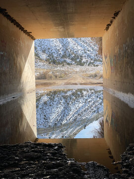 Mountain Reflection Beneath a Rural Underpass in Winter, A quiet dirt road emerges from a concrete underpass