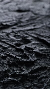 Dark cracked rough texture slow pan. Close-up of deep black rough surface with irregular cracks and relief. Smooth linear camera movement reveals shifting light and shadow across the textured details.