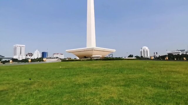 Slow cinematic view of the National Monument (Monas), Jakarta, Indonesia, under a clear blue sky. Ideal for travel, tourism, architecture, heritage and educational projects.