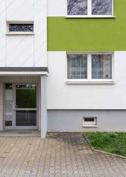 Residential building entrance facade with white siding and a bright green painted accent band around white framed windows next to a glass door.