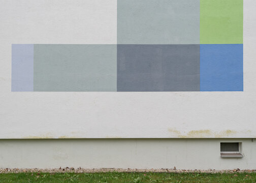 Geometric abstract frame of a building foundation wall featuring colored rectangles in grey, blue, and green shades above a lawn.