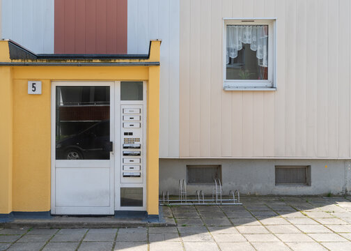 Minimalist graphic architectural view of a pale green plastered residential wall painted with the house numbers 9a-11a next to contrasting vertical brown panels.