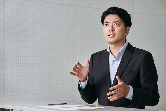 相手の目を見てデスクでプレゼンを行いながら話す30代の日本人の男性の会社員
