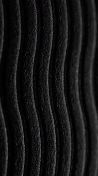Black wavy ribbed texture slow pan. Close-up of deep black textured surface with vertical wavy ridges. Smooth linear camera movement reveals shifting light and shadow across the pattern.