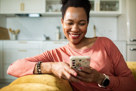 Smiling woman using smartphone on couch in home kitchen