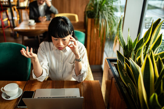 Concerned woman on phone working on laptop in cafe
