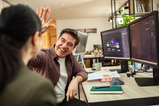 Coworkers high-fiving after project success in modern office