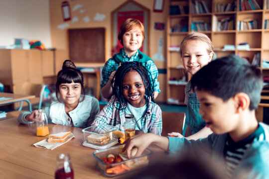Happy schoolchildren eating lunch together in classroom