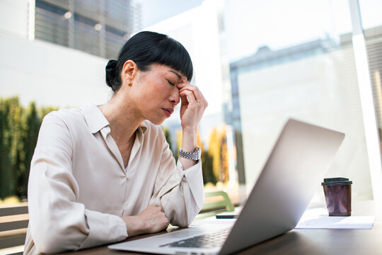 Tired businesswoman rubbing eyes while working on laptop outdoors