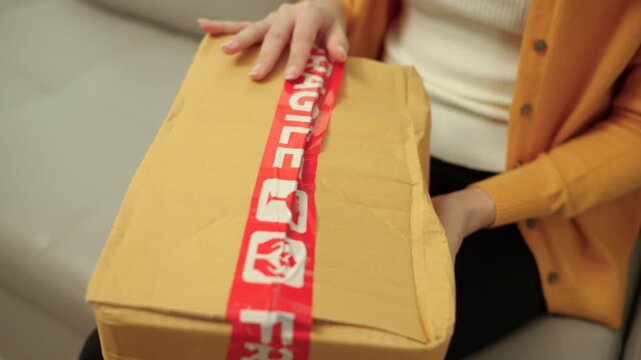 Close up Stressed young woman looking at a damaged parcel after online shopping at home. Broken package shipping damage or delivery problem. E-commerce, consumer rights and insurance claim concept.
