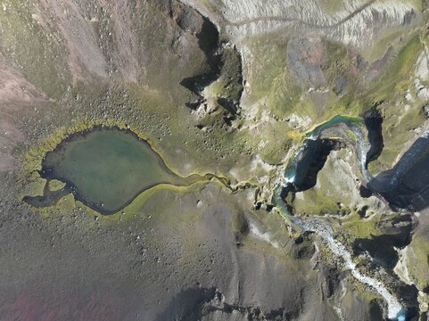 Aerial view of Raudibotn crater lake with vibrant green moss, dark volcanic rock, and a winding stream in the rugged terrain of Svartafellstangi, Skaftarhreppur, Iceland.