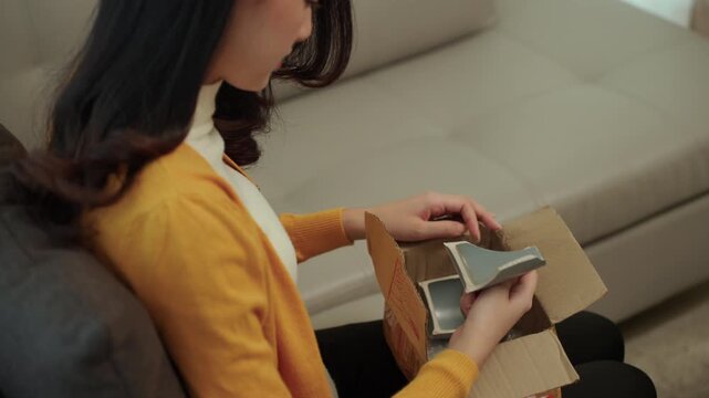 Close-up Stressed young woman opening a parcel and discovering damaged product after online shopping at home. Shipping damage, delivery issue. E-commerce, consumer rights and insurance claim concept.
