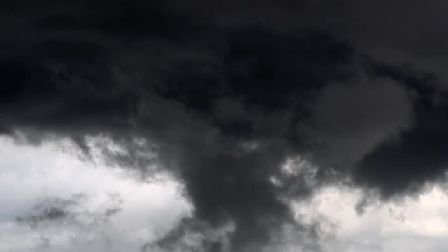 Ominous, swirling black clouds against a gray sky&mdash;a dramatic darkness associated with rain or a storm.