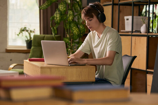 Teen boy studying with laptop and headphones at home desk. Concept of online learning, remote school, study routine, digital skills and home workspace.