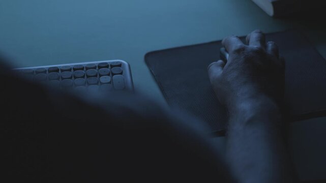 Developer working on a code at night, close-up of hand on mouse