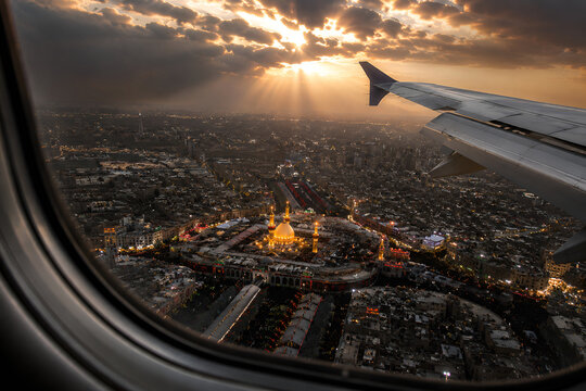 Airplane Window View Over the Holy City of Karbala at Sunset with Golden Shrine and Dramatic Sun Rays
