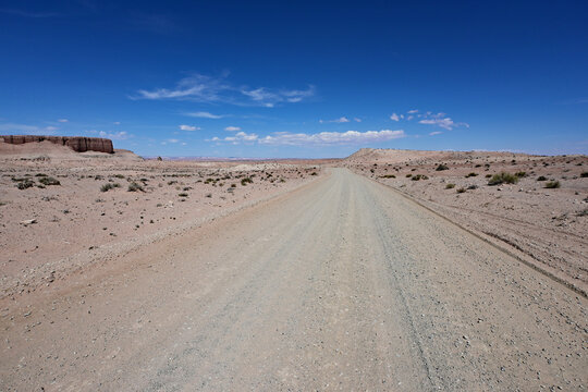 Desert dirt road receding into distance under bright blue skies and light white clouds near Hanksville in south central Utah.