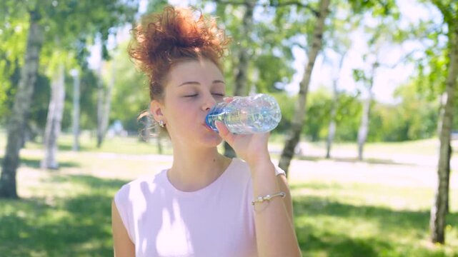 A young woman is drinking water in the park