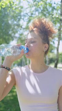 A young woman is drinking water in the park