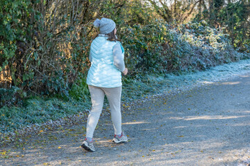 Fototapeta premium away from the camera on frosty park path early in morning, back view active lifestyle and healthy aging sports in nature during cold weather, winter jogging motivation, healthier routine in nature