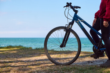 Fototapeta premium Young adult person standing with blue bicycle near ocean shore under clear sky