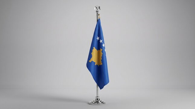 The national flag of Kosovo, featuring a blue field with a golden map of the country and six white stars, stands on a flagpole against a light grey background.
