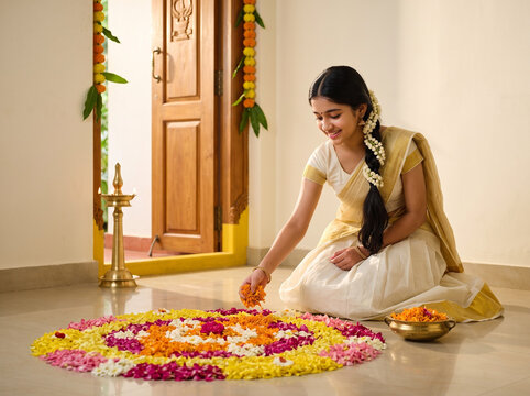young indian girl in traditional kerala kasavu pavada creating colorful onam pookalam at home entrance during festive celebrations