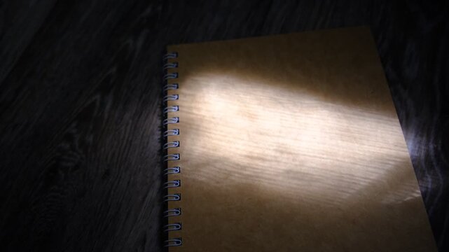 Notebook with a blank cover page. Sunlight, rays creates dynamic highlights, shadows across the paper. Creativity, planning, new beginnings, brainstorming.  Education, writing, design-related content.