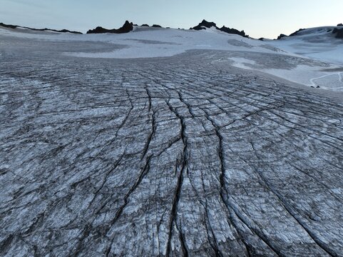 Aerial view of the deep crevasses and icy surface of the glacier with rugged mountain peaks in the background in Kalfafellsstadur, Hornafjordur, Iceland.