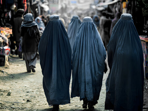 Group of women in blue burqas walking together through a bustling market street with vendors and shoppers visible in the background