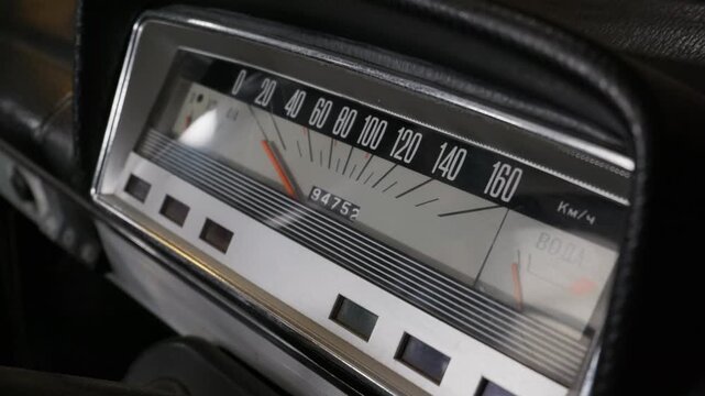 An analog speedometer of a classic car shows speed and mileage. The cluster features retro styling with Cyrillic text and mechanical needles. Warm light illuminates the dashboard.