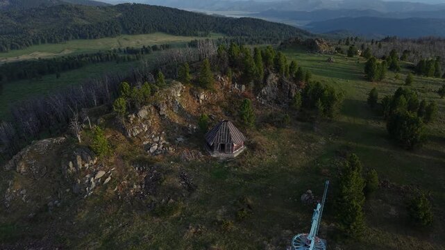 Cinematic drone aerial rising shot moving backwards from a wooden mountain cabin, revealing a majestic panorama of vast cedar forests and distant Altai mountain peaks at golden hour sunset.